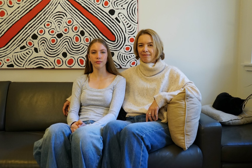 A teenage girl and a woman sit on a couch next to each other