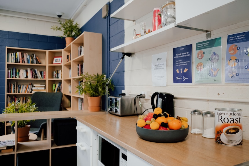 The living and kitchen area of a residential facility. There's a bookshelf and bright colours on the walls.