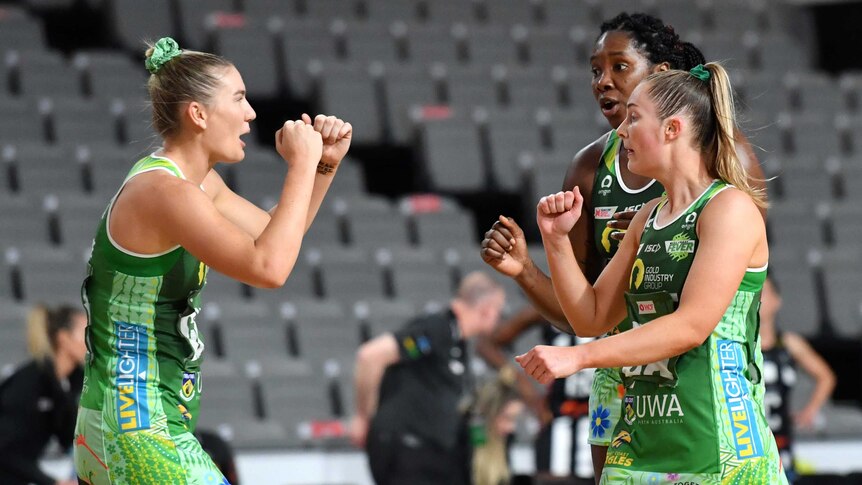 Three Super Netball teammates get set to bump fists in celebration after a goal.