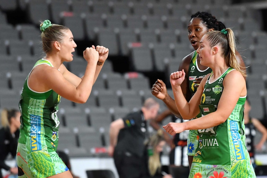 Three Super Netball teammates get set to bump fists in celebration after a goal.
