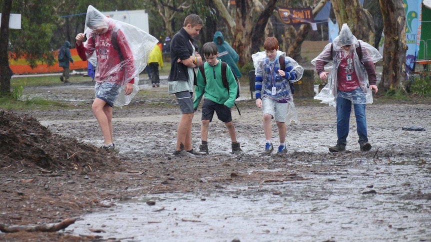 Scouts wearing clear plastic raincoats tramp through mud at the Australian Jamboree.