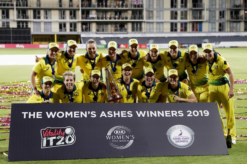 A group of smiling cricketers celebrate with the trophy at the end of the Women's Ashes series.