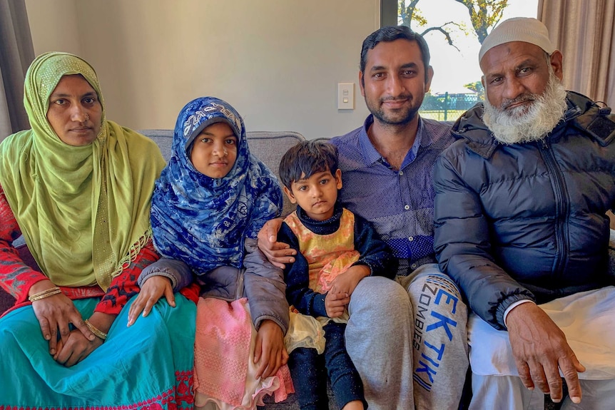 Two men, and woman and two children sit on a couch together