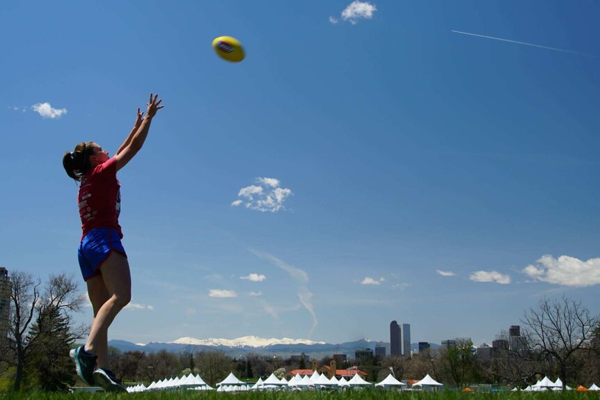Sara Edwards Rohner jumps to mark a football with snow-capped mountains in the background.