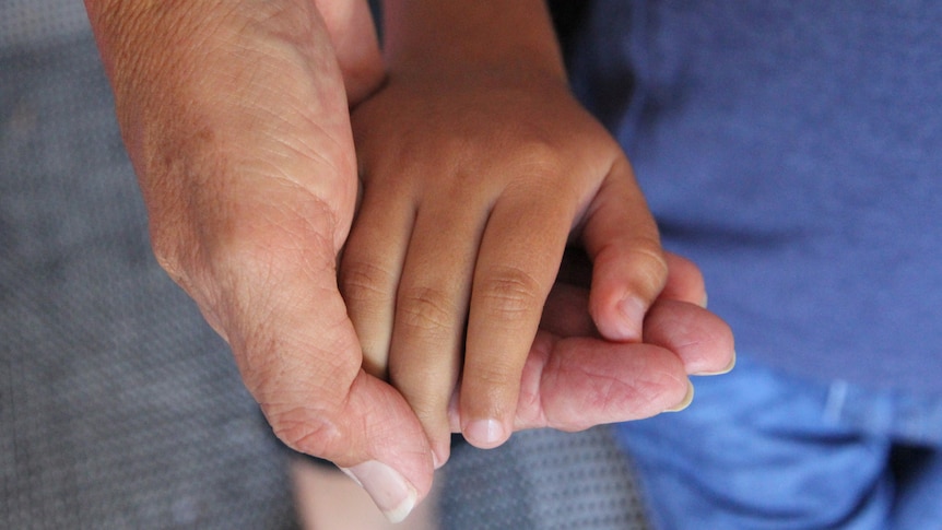 A small child's hand is cupped by an old woman's hand
