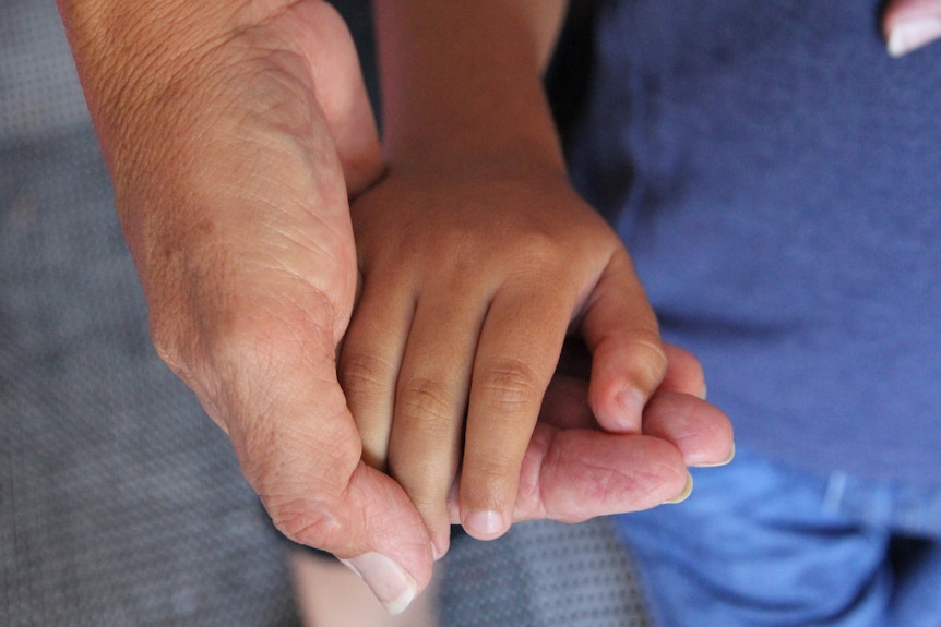 A small child's hand is cupped by an old woman's hand