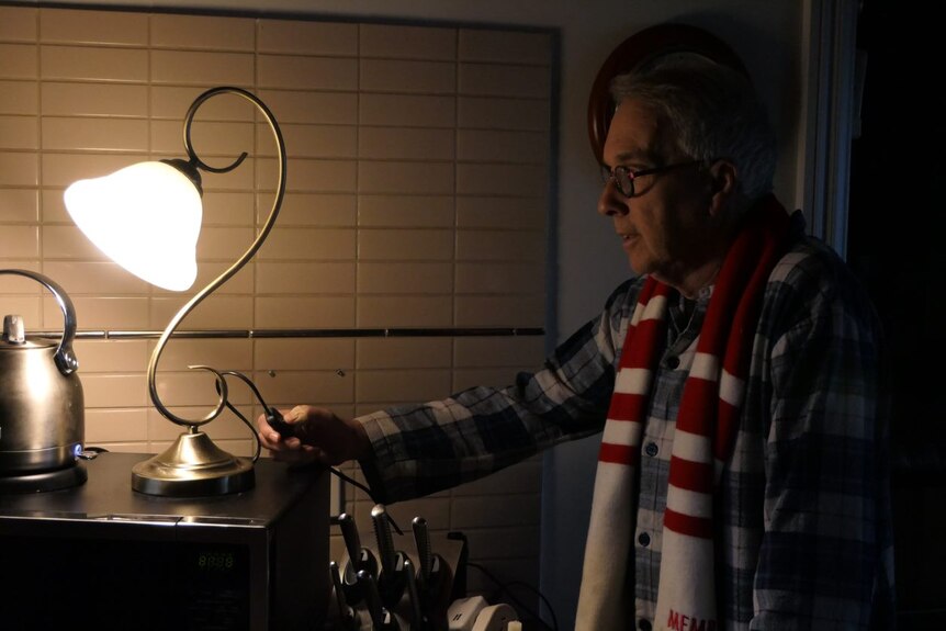 A man switches on a small table lamp.