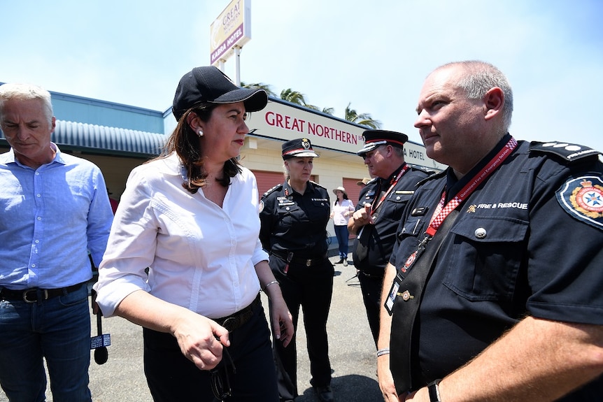 A woman wearing a cap chats with an emergency services officer outside a pub.