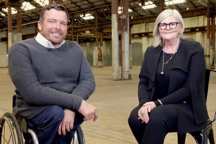 Sam Mostyn and Kurt Fearnley sit next to each other and smile for a photo