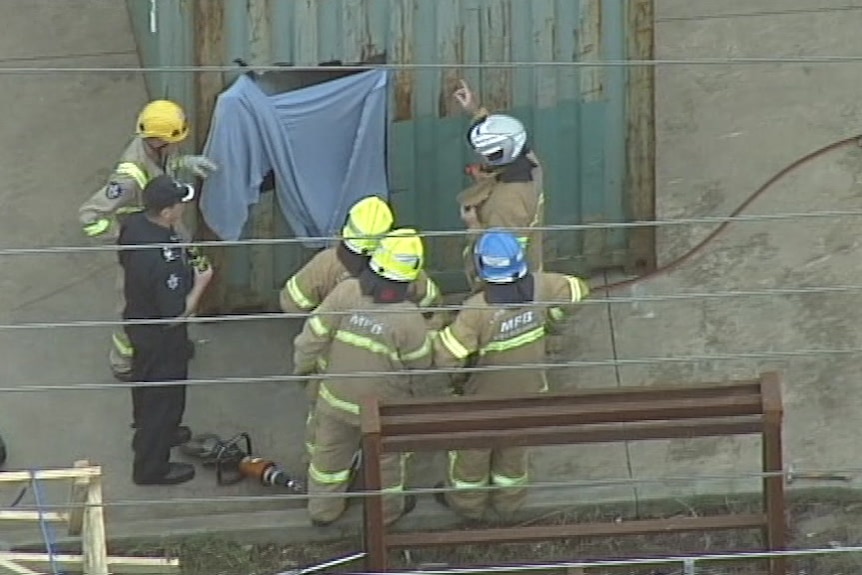 Emergency services workers stand around a hole cut in the end of a shipping container.