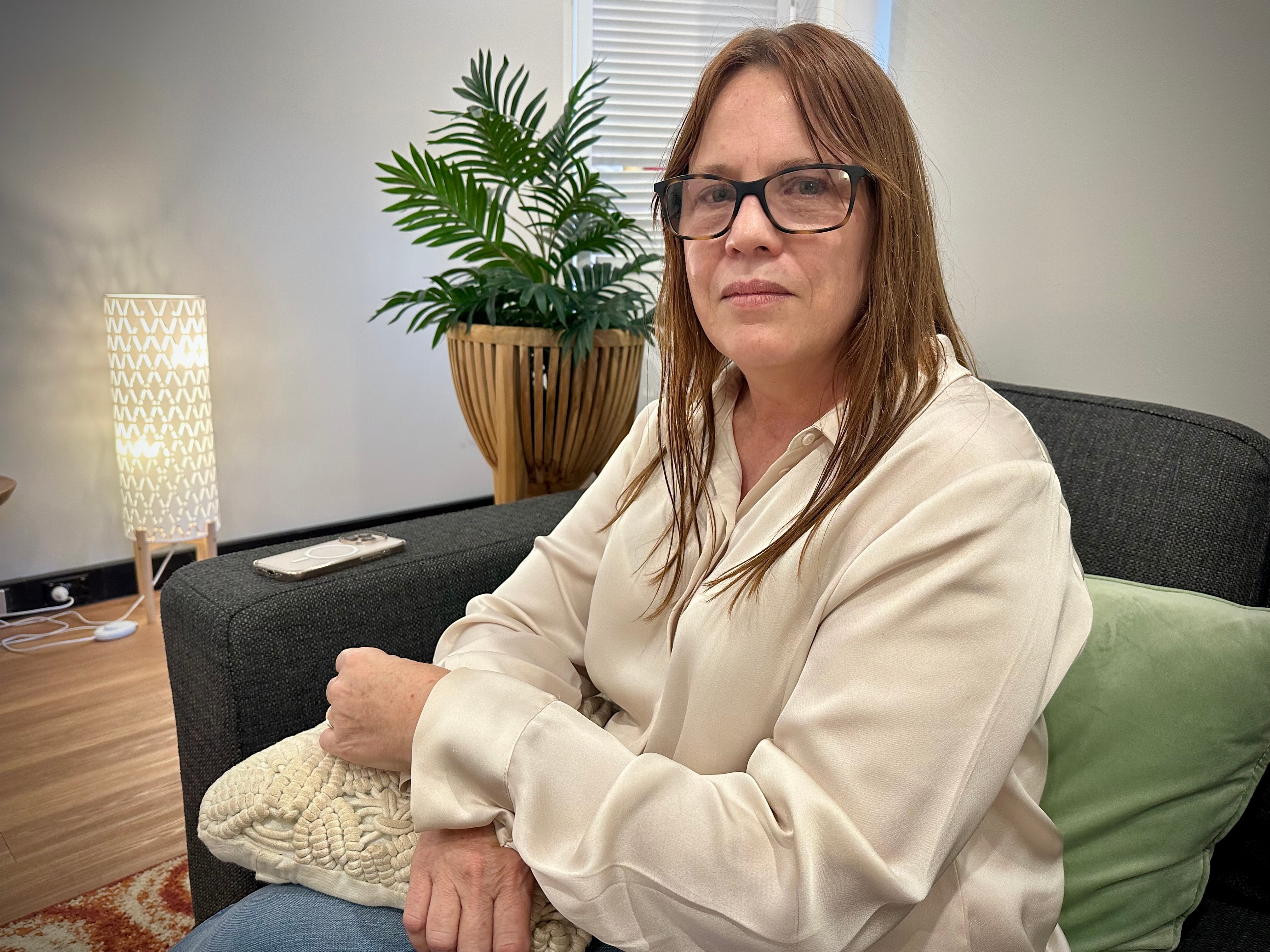 Una mujer sentada en un sofá y mira a la cámara.