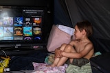 A child sitting in front of a TV screen, looking towards the screen.