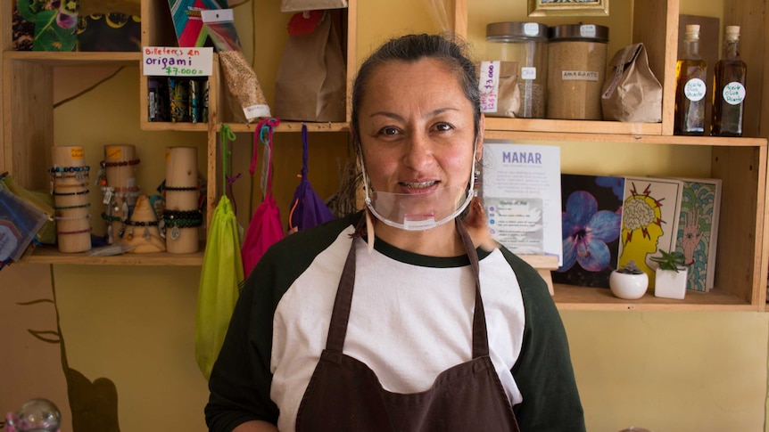 A woman in a black and white t-shirt with a clear plastic mask and jars of food behind her