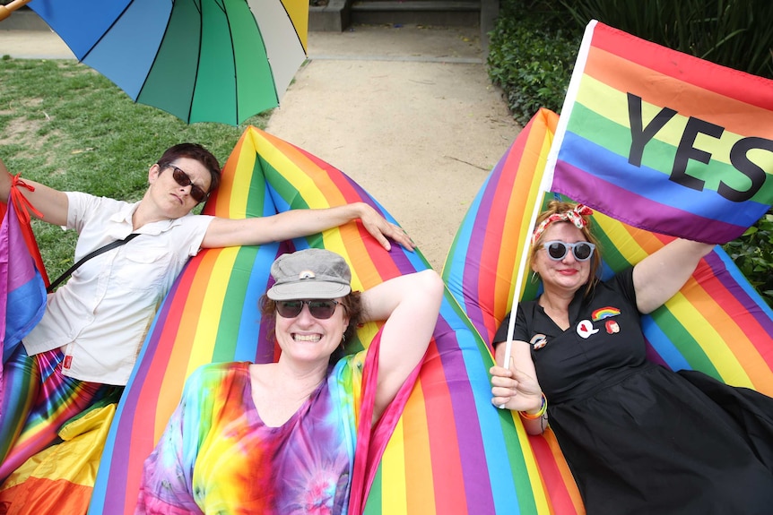Caitlin, Megan and Suzette lounging on rainbow seats with rainbow flags at the State Library.
