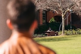 A photo of the blurred back of a man's head and shoulders. The picture looks at someone sitting at a bench in the d