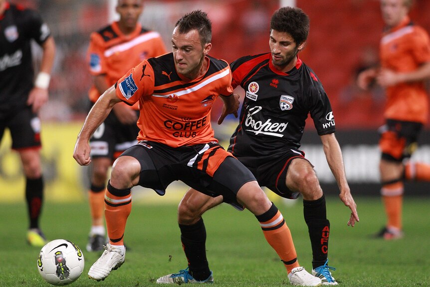 A Brisbane Roar players shields the ball from an Adelaide United player on the field of a soccer game.