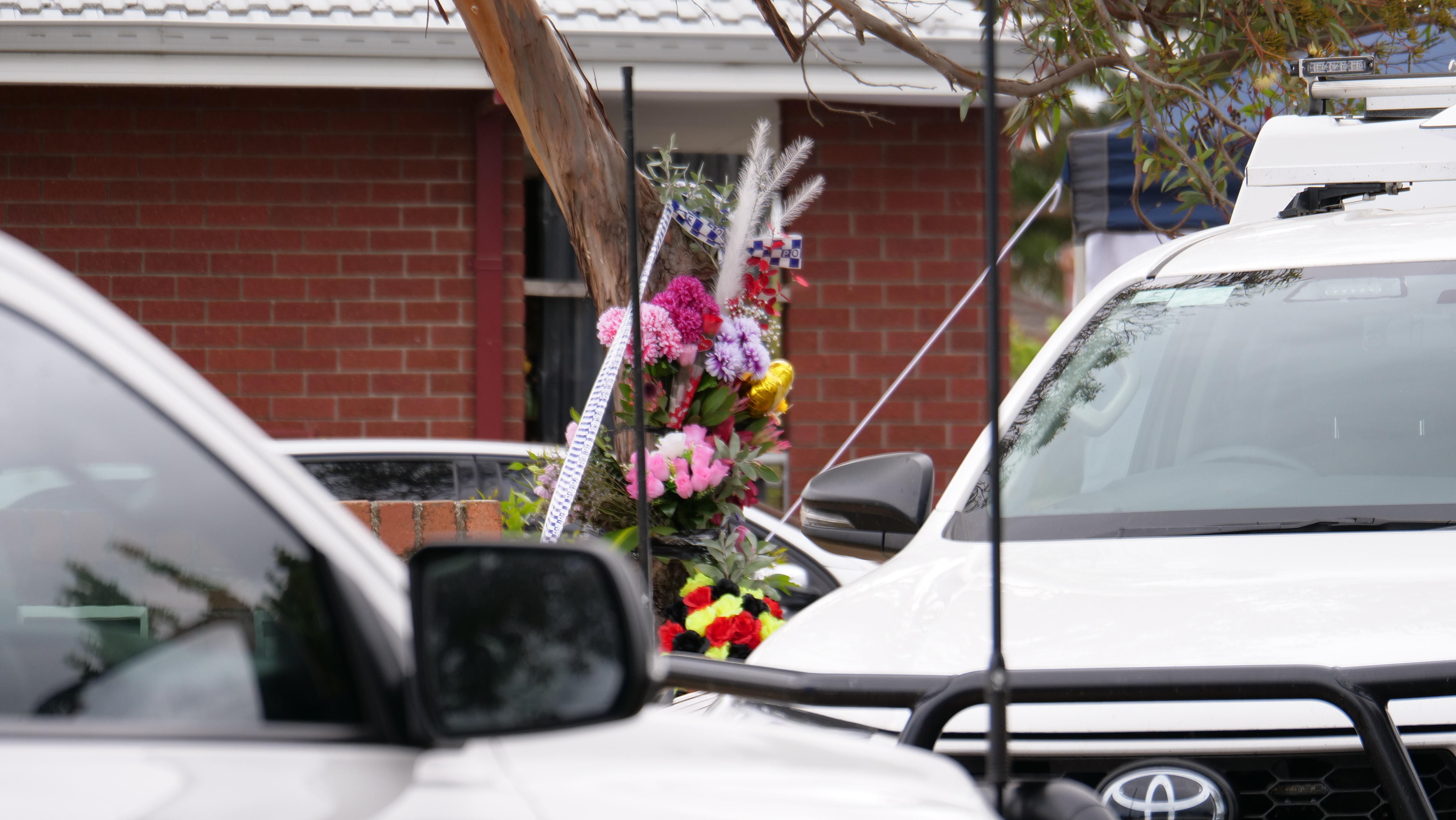 Flores pegadas a un árbol junto a la cinta policial. 