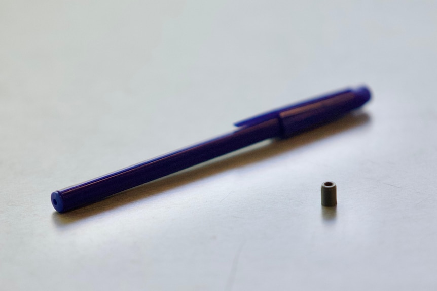 A 3D printed replica of a missing radioactive capsule next to a pen on a table.