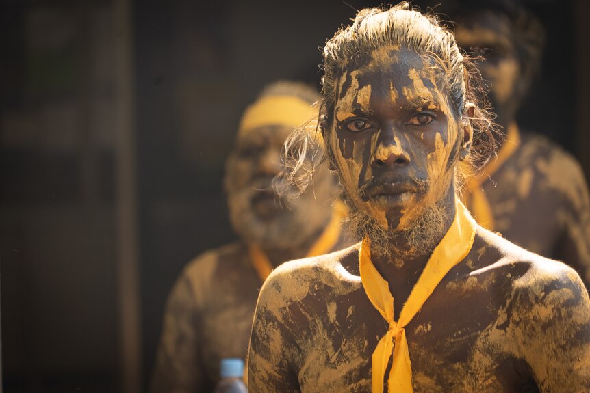 A man wearing body and face paint looking into the distance at a ceremony in Wadeye.