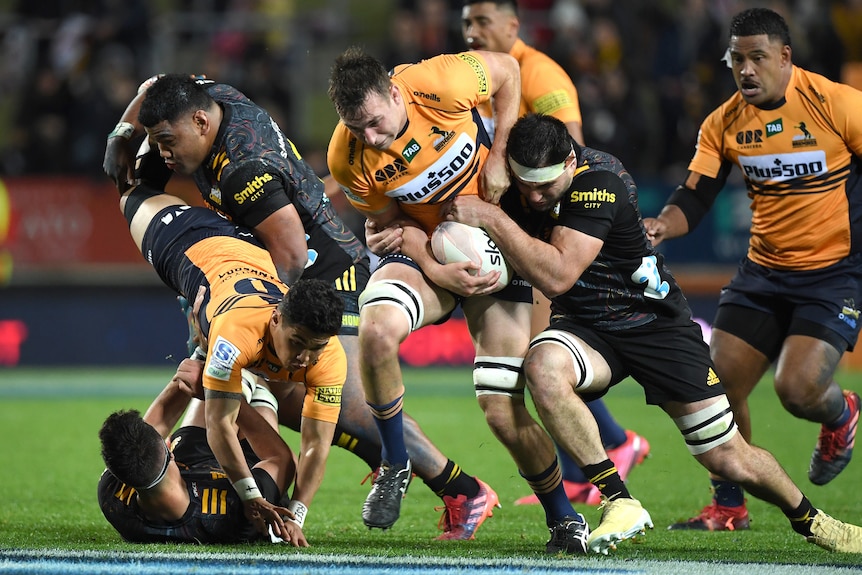 Rugby player running the ball with the opposition team trying to tackle him during a match