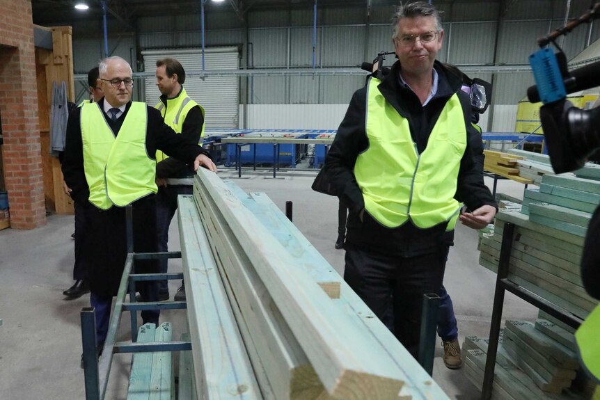 Malcolm Turnbull wearing a high-vis vest and holding a wooden beam at a factory in the ACT.