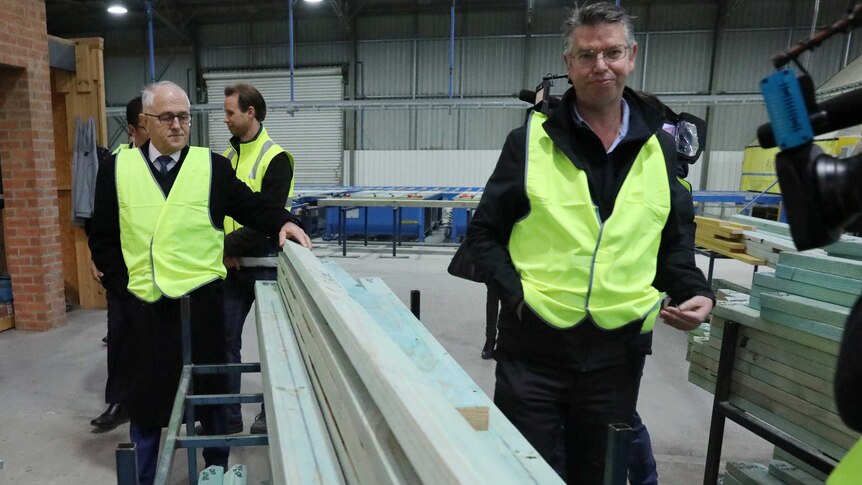 Malcolm Turnbull wearing a high-vis vest and holding a wooden beam at a factory in the ACT.