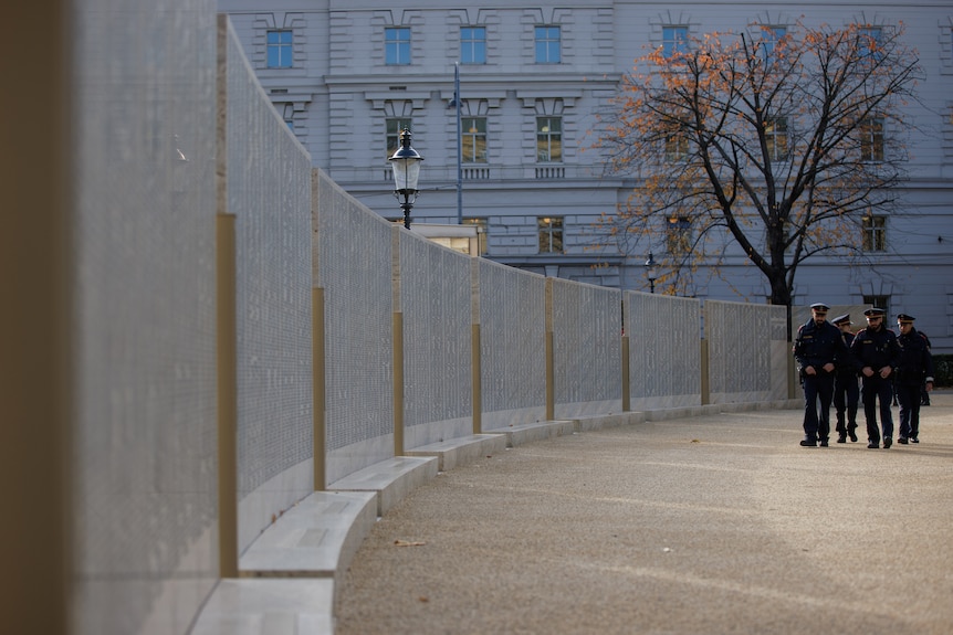 Police officers walk next to a wall.