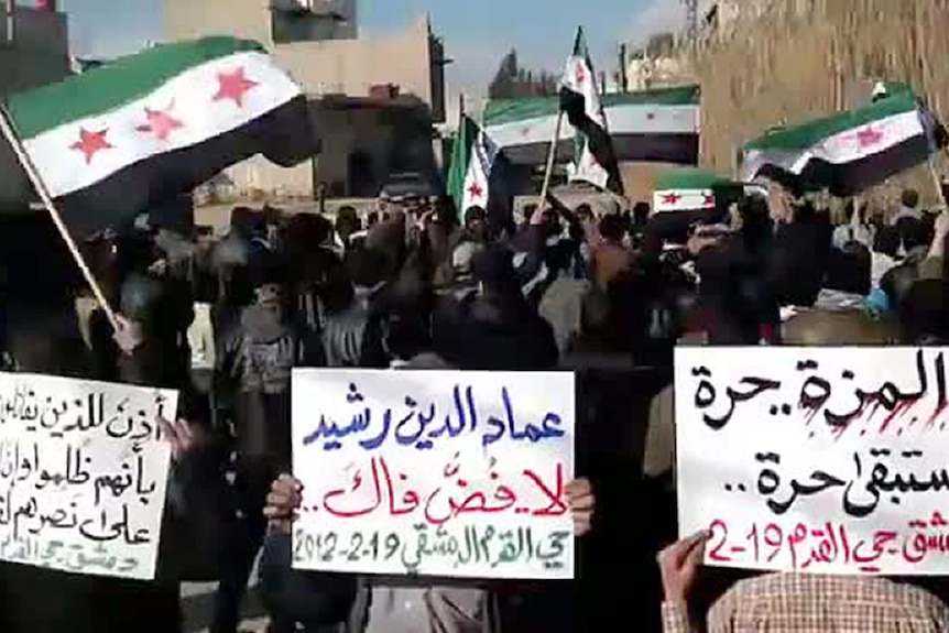 Syrians wave the former pre-Baath flag as others hold slogans during an anti-regime protest.