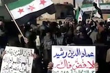 Syrians wave the former pre-Baath flag as others hold slogans during an anti-regime protest.