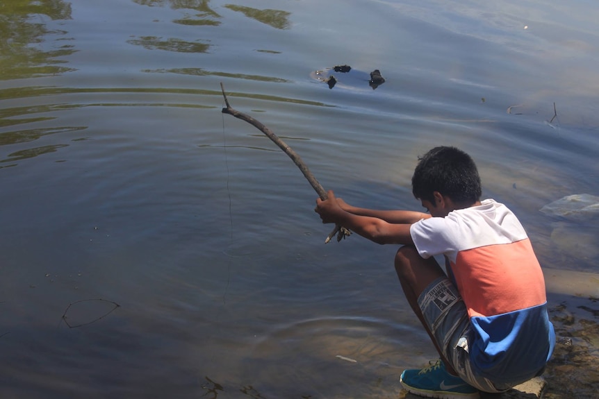a young child holds a stick with a fishing line over water
