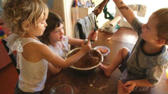 Children play with cake mix in a kitchen.