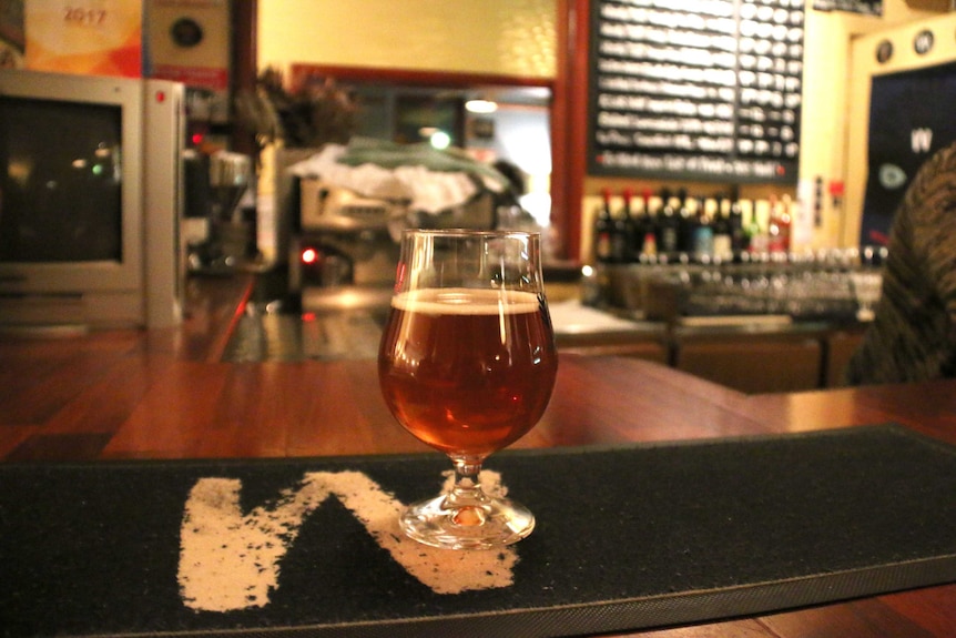 A glass filled with beer sits on a bar.