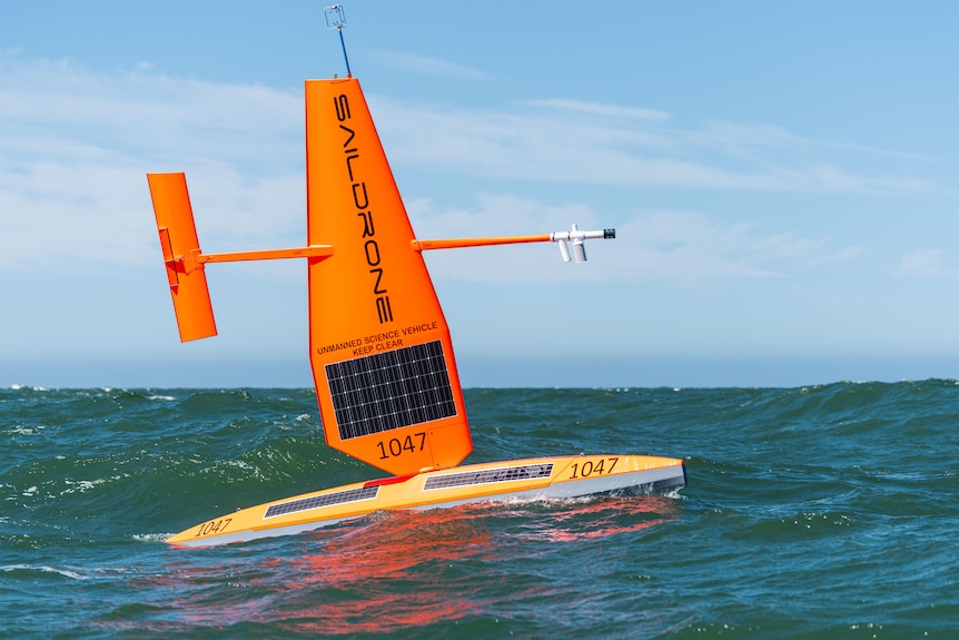 Orange vessel the size of a windsurfer in the ocean with solar panels