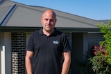 Matt Emptage in a black polo shirt stands outside his house.