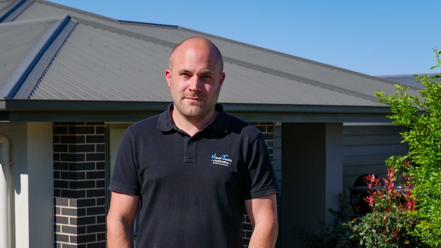 Matt Emptage in a black polo shirt stands outside his house.