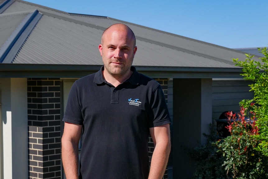 Matt Emptage in a black polo shirt stands outside his house.