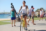 A woman on a bright yellow bike cycling on a footpath in front of a beach