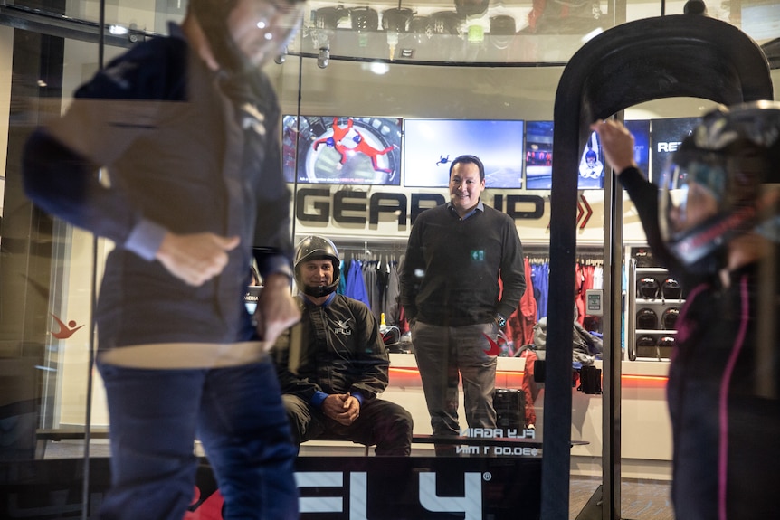 A man watches on as people stand inside a controlled indoor skydiving centre 