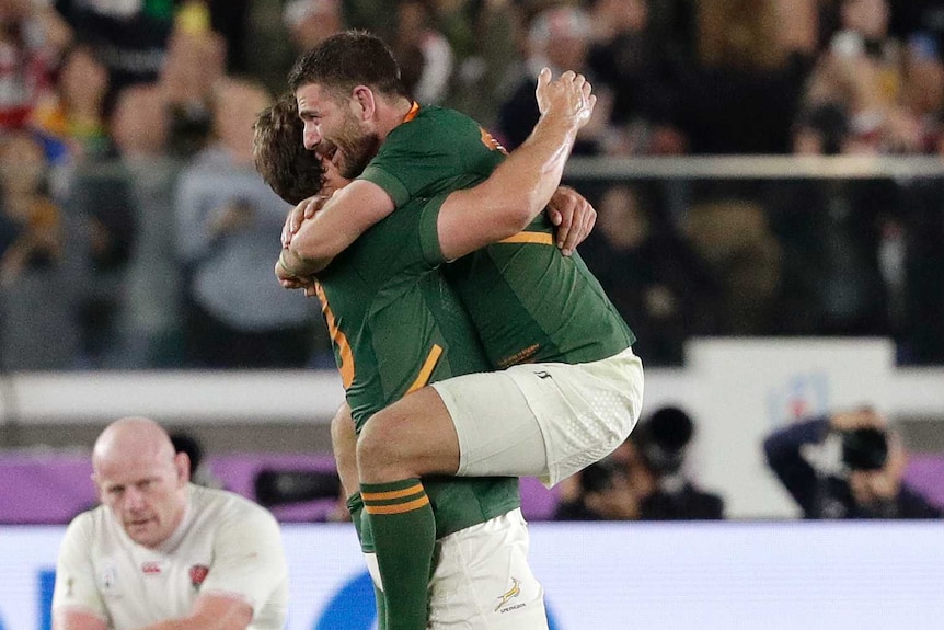 Handre Pollard jumps into the arms of his Springboks teammate Franz Steyn. There are happy Springboks and sad Englishmen nearby.