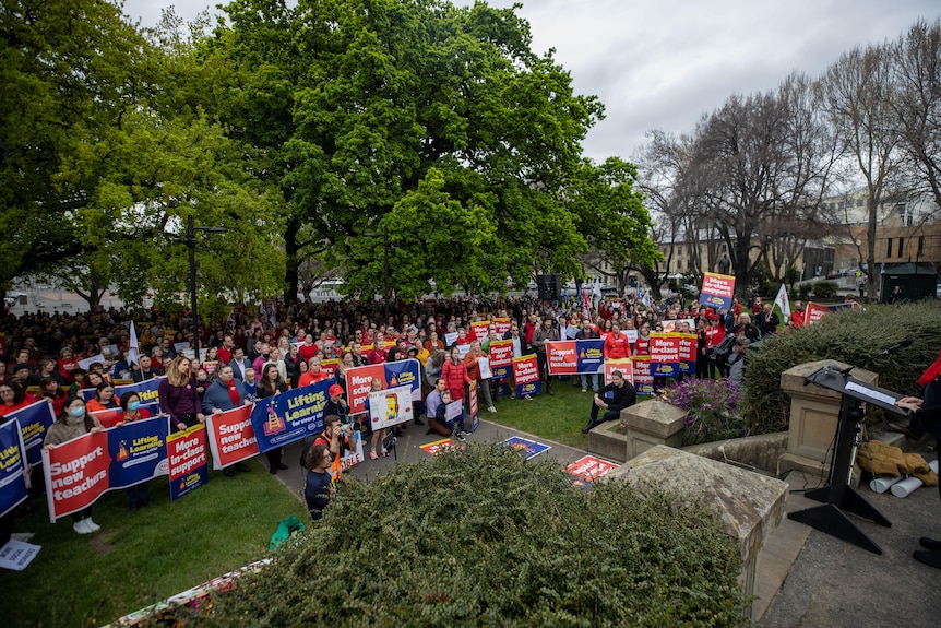 A large group of people, many holding banners and placard, in a park.