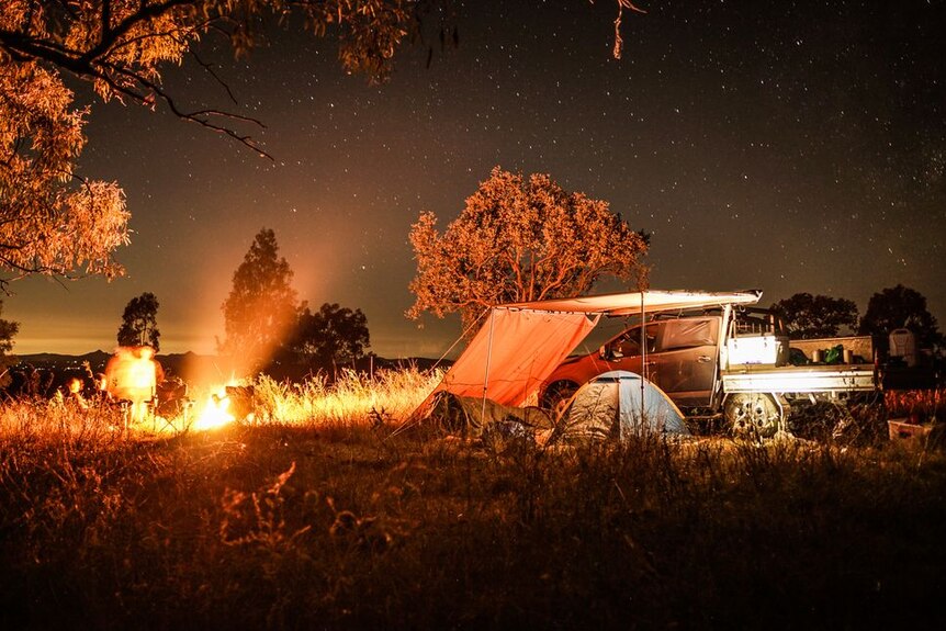 Stunning photo of a campsite under the stars with a glowing camp fire.