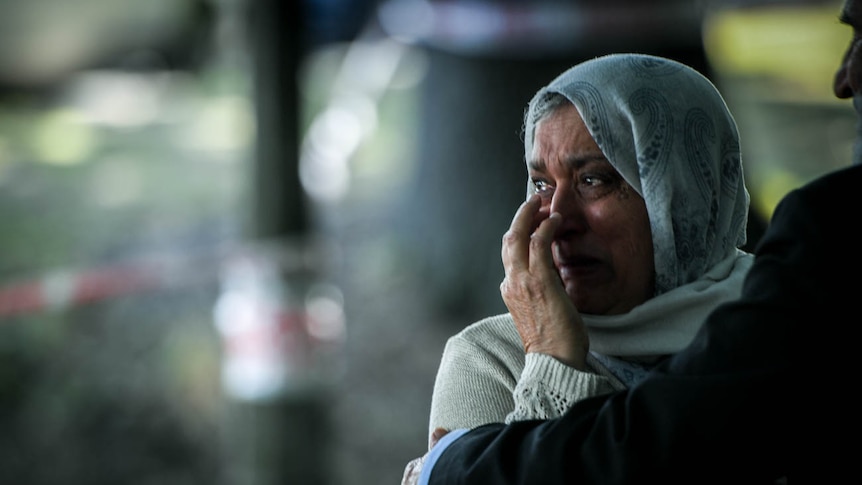 A women holds her hand to her face as tears stream down her checks.