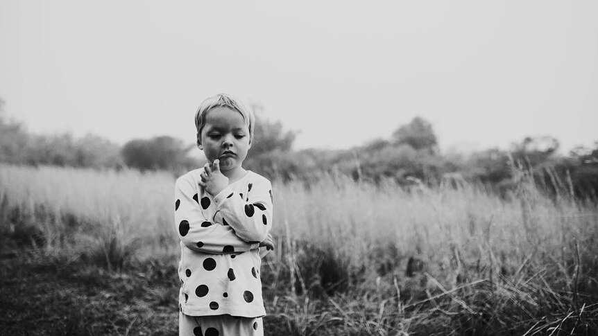 A young boy, wearing spotty pyjamas frowns.