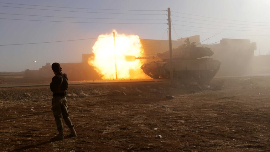 A rebel fighter stands near a Turkish tank as it fires towards Aleppo.