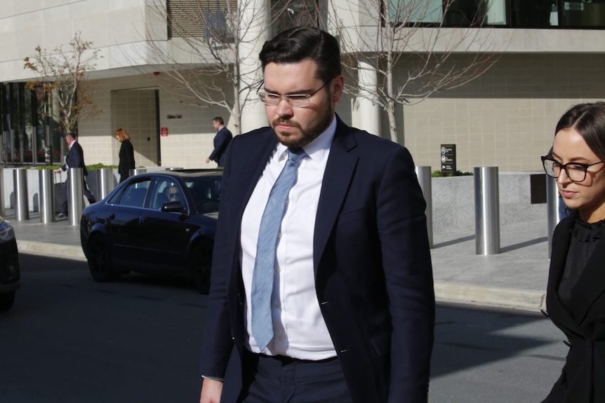 A man in a blue suit and tie walks out of a courthouse.