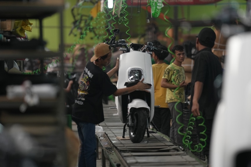A motorcycle on a conveyer belt with men adding parts.