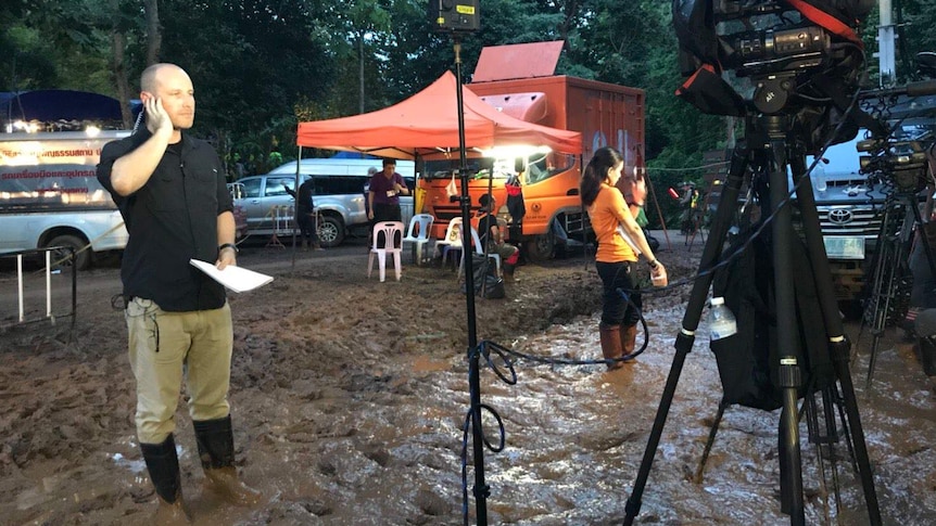 Cochrane wearing gumboots standing in mud holding hand to earpiece and looking at camera ready for cross.