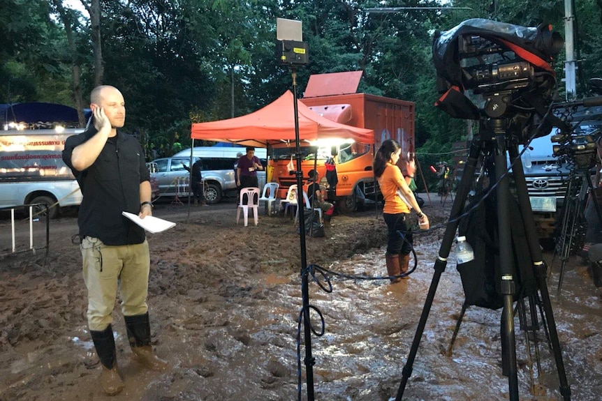 Cochrane wearing gumboots standing in mud holding hand to earpiece and looking at camera ready for cross.