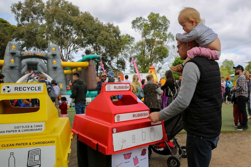 Man carrying child on his shoulders puts rubbish into a bin at a school fete.