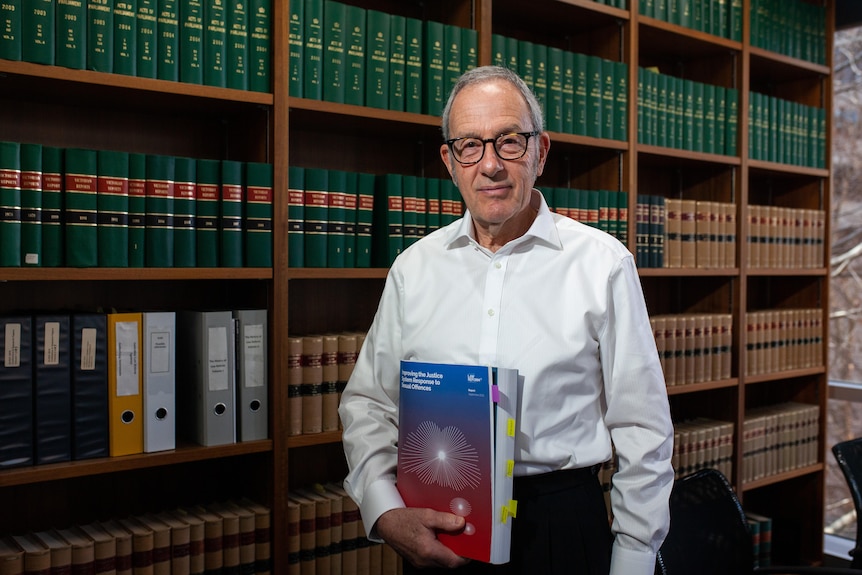 A man holding a report and standing in front of a bookshelf of legal texts.